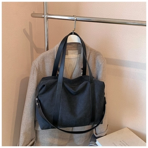 Dettaglio della borsa tote nera in tela con manici in pelle appesa a un supporto metallico