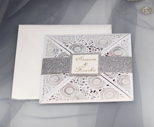 Detail of laser-cut floral wedding invitation with silver glitter belt and white envelope