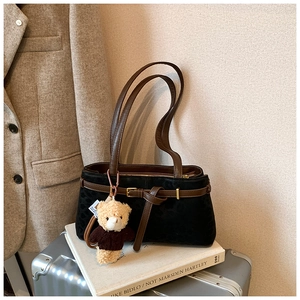 Detail of black suede bucket bag with leather strap and a cute brown plush bear charm