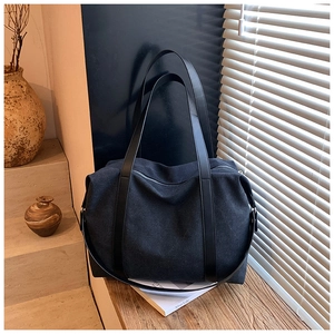 Detail of a black canvas tote bag with leather straps and metal zipper on a wooden ledge