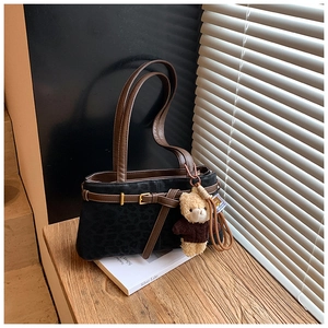 Close-up of black leopard embossed suede bucket bag with leather strap and bear charm