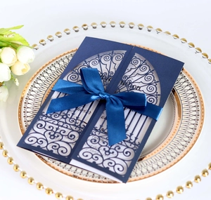 Macro shot of navy blue laser cut wedding invitation with ribbon on porcelain tray