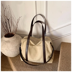 Detailed view of beige canvas tote bag with brown leather handles in a warm studio setting