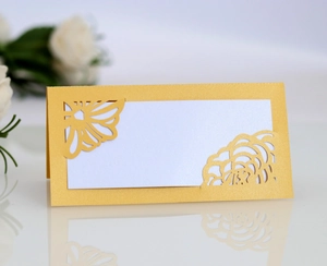 Detail of laser-cut gold hollow place card with butterfly pattern on white table