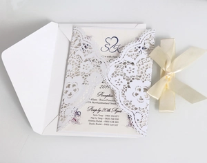 Close-up of laser-cut lace wedding invitation with a cream satin bow and navy text