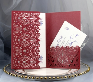 Close-up of burgundy laser-cut lace wedding invitation with floral insert and gold tray