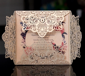 Laser-cut champagne gold floral wedding invitation with vintage inner card on a reflective surface