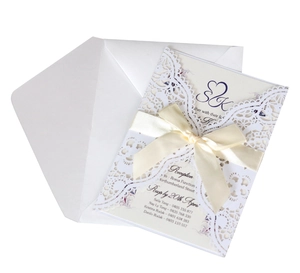 Detail of white laser-cut lace wedding invitation with cream ribbon bow and inner card