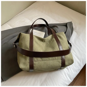 Detail of green canvas tote bag with brown leather straps on a grey blazer backdrop