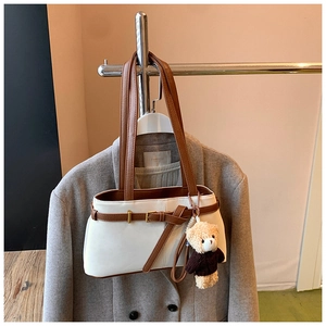 Detail of white leather shoulder bag with brown straps and cute plush bear keychain charm