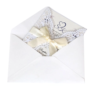 Detail of laser-cut lace wedding invitation with a beige silk ribbon bow and inner card
