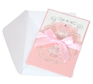 Detail of pink laser-cut invitation card with lace pattern and silk ribbon bow