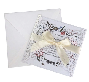 Détail d'une invitation de mariage découpée au laser avec nœud crème et carte florale
