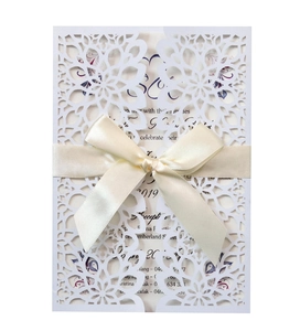 Macro detail of laser-cut floral wedding invitation with cream satin ribbon and insert
