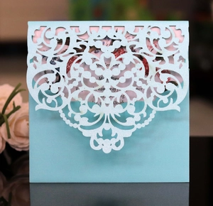 Macro detail of laser-cut hollow blue floral pattern invitation with pink inner card