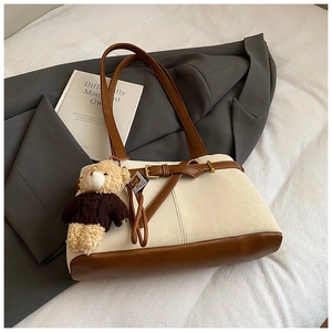 Detail of a contrast tote bag with a bear charm and gold buckle on a white bed sheet