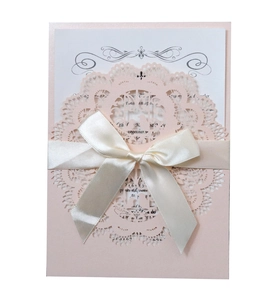 Detail of pink laser-cut wedding invitation with lace patterns and cream ribbon bow