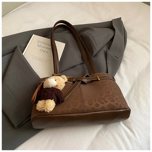 Detail of dark brown leather bucket bag with leopard texture and teddy bear charm