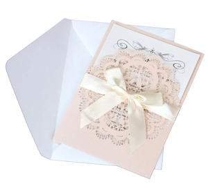 Detail of laser-cut wedding invitation featuring pink bird lace and cream ribbon bow