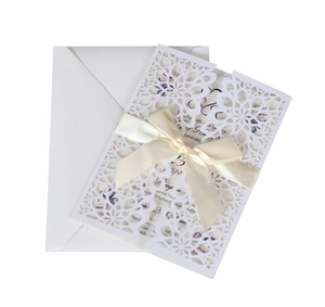 Detail view of laser-cut floral wedding invitation with cream silk ribbon and white envelope