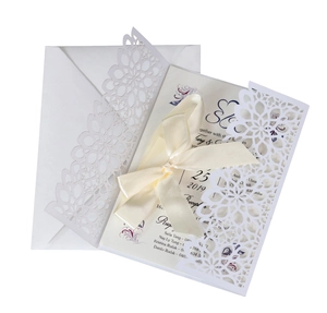 Detail of laser-cut floral wedding invitation with cream ribbon and white envelope set