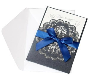 Macro shot of laser-cut lace invitation with a blue satin ribbon and elegant printed insert