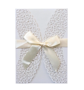 Close-up of laser-cut floral wedding invitation cover with elegant cream satin ribbon bow
