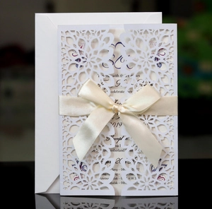 Detail of laser-cut floral wedding invitation with cream ribbon bow and inner card