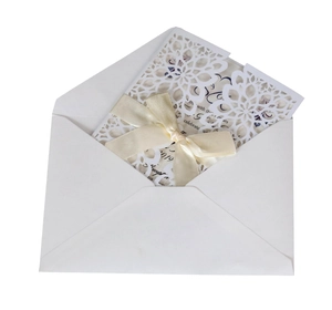 Detail view of laser-cut floral wedding invitation with beige ribbon bow and white envelope