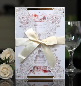 Close-up of laser-cut wedding invitation with beige silk ribbon and floral inner card