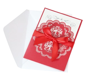 Close-up of laser-cut wedding invitation with white inner card and red satin bow