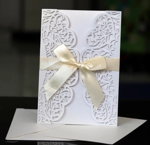 Detail of laser-cut white wedding invitation with champagne silk ribbon and hollow floral patterns