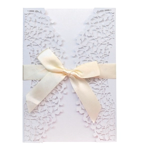 Detail of laser-cut leaf pattern on white invitation card with a silk ribbon bow
