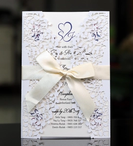 Intricate laser-cut leaf pattern on white wedding invitation with a beige satin bow