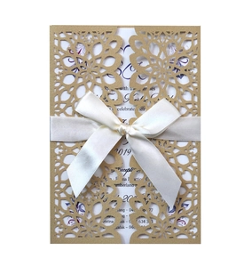 Detail of laser-cut floral wedding invitation with cream satin ribbon and bow