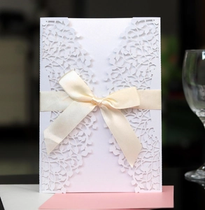 Detail of laser-cut leaf pattern on white wedding invitation with a beige silk bow