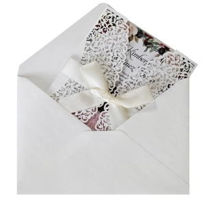 Detail of laser-cut wedding invitation with intricate floral pattern and white satin bow