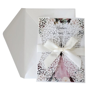 Close-up of laser-cut wedding invitation with white ribbon and floral inner card