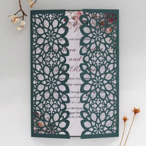 Detail of dark green laser cut wedding invitation with floral insert card on a desk