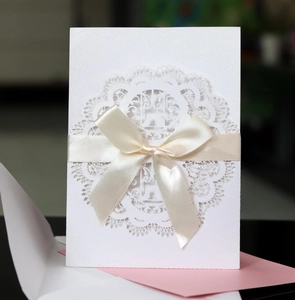 Detail of laser-cut lace pattern on white pearl paper card with satin bow and envelopes