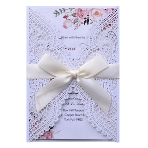 Detail of laser-cut white lace wedding invitation with cream satin bow and floral insert