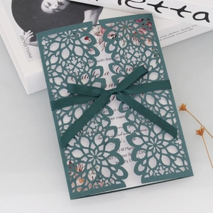 Detailed macro view of laser-cut floral wedding invitation with green silk ribbon bow