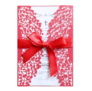 Detail of red laser-cut wedding invitation with elegant vine patterns and a silk ribbon