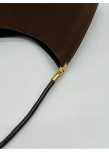 Detailed close-up of dark brown suede bucket bag with black strap and golden metal hook