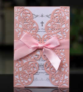 Detail of pink laser-cut wedding invitation with white insert and satin ribbon bow