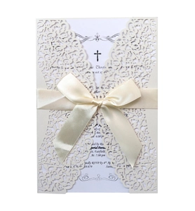 Detail of laser-cut invitation with ivory floral pattern, white ribbon, and cross design