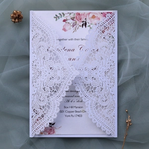 Close-up of laser cut white lace wedding invitation with floral insert and elegant textures