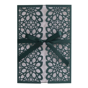 Detail of laser-cut floral wedding invitation with dark green cover and silk ribbon bow