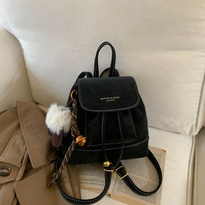 Detail of black leather backpack with white stitching and plush ball on a sofa