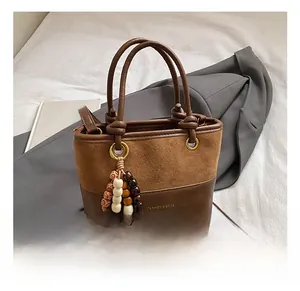 Detail view of brown bucket bag with beaded charm and gold logo lettering